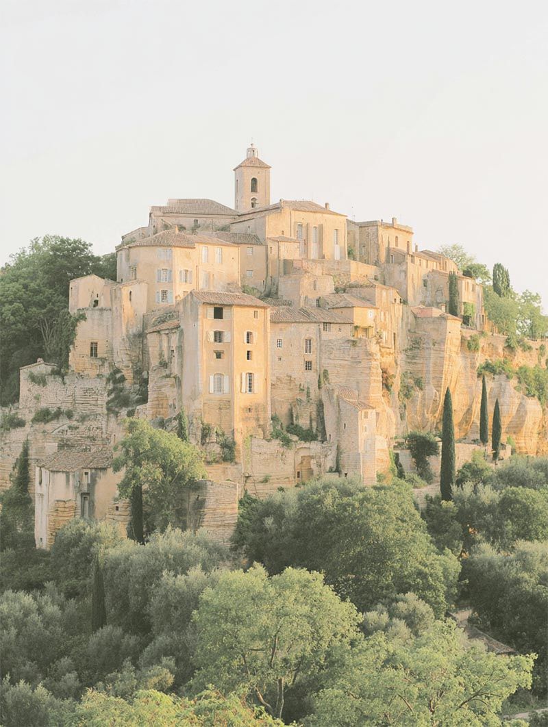 Rustic hilltop Provençal village perched on a cliffside at golden hour, a luxury destination wedding venue surrounded by cypress trees