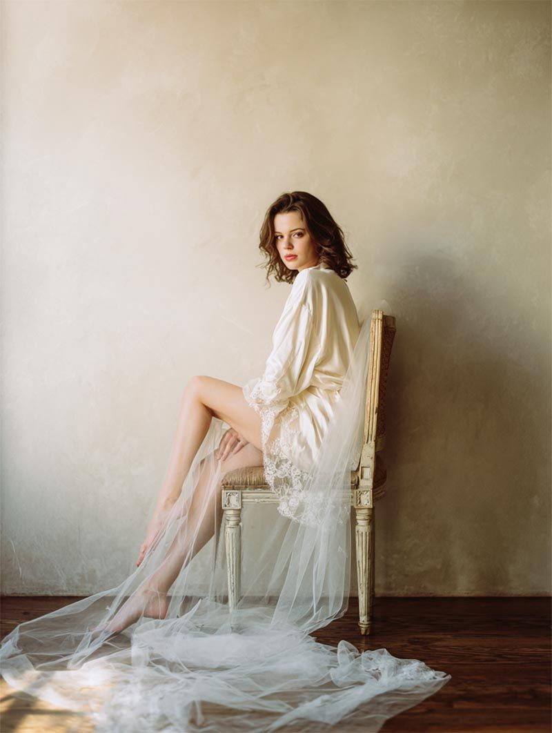Bride in silk robe on vintage chair with cathedral veil, Michigan Luxury Weddings portfolio